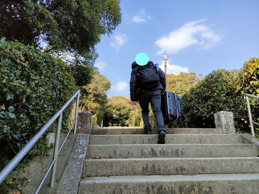 志賀海神社の参道をキャリーケースを持って歩く男性